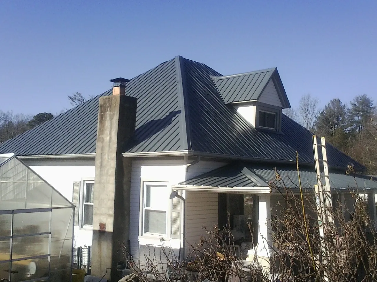 Dark blue standing seam metal roof on a white farmhouse with dormer — Slate & Tile Roof Repair by Roofing Brothers in Pursglove