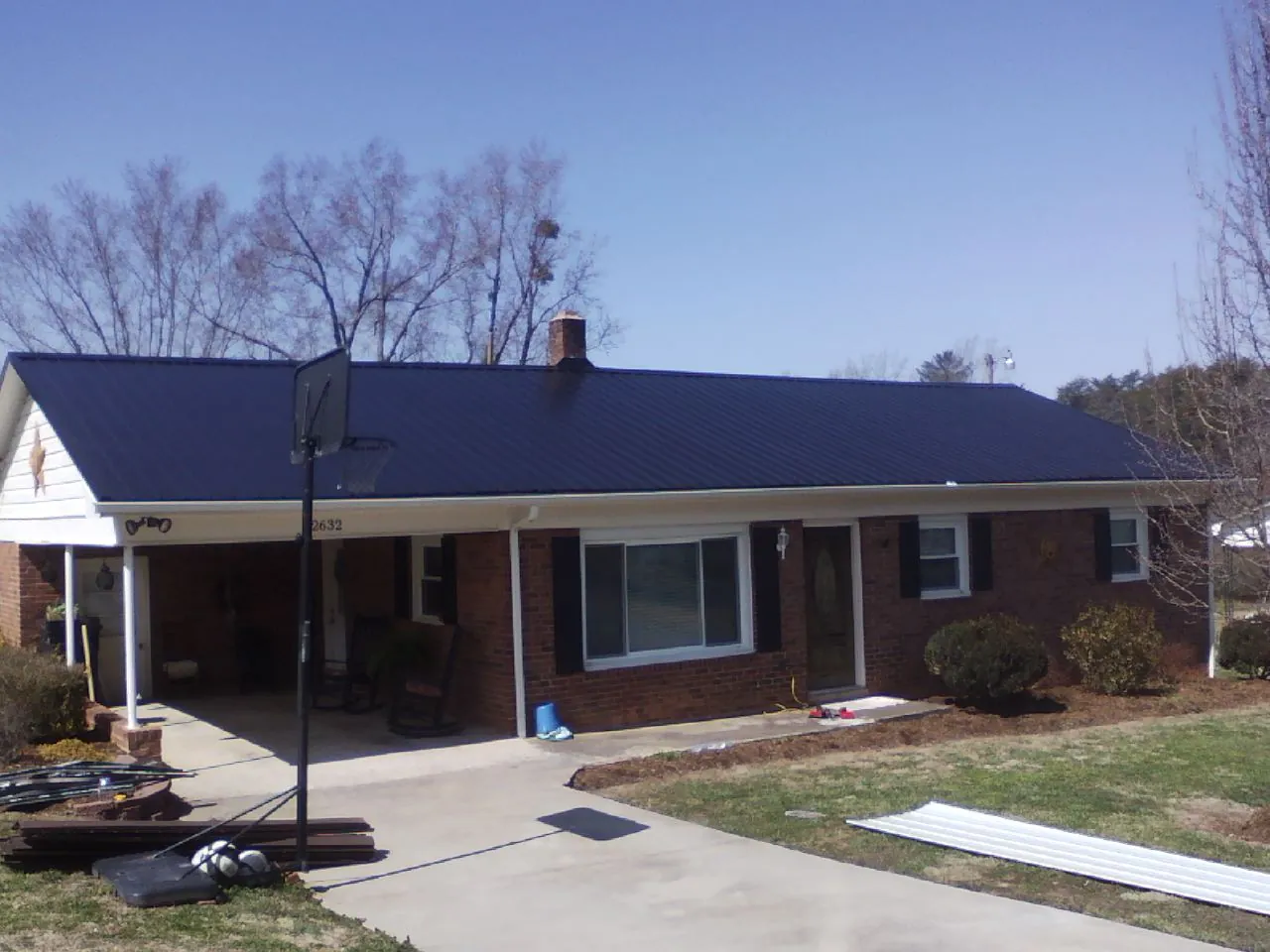 Finished dark blue metal roof on a brick ranch with a carport in Pursglove