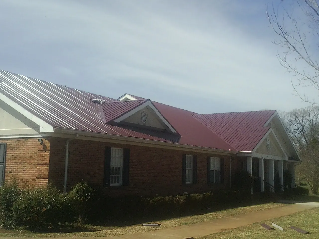 Red metal roof with gabled entries on a long brick building, from a Hail Damage Roof Repair job in Pursglove