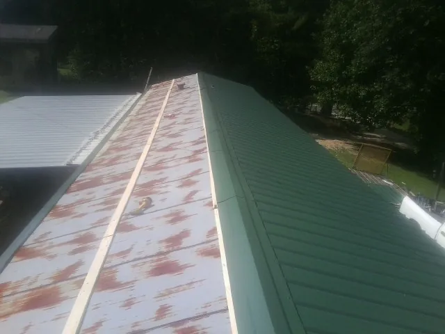 Old rusted panels beside newly installed green metal roofing — Wind Damage Roof Repair by Roofing Brothers in Pursglove