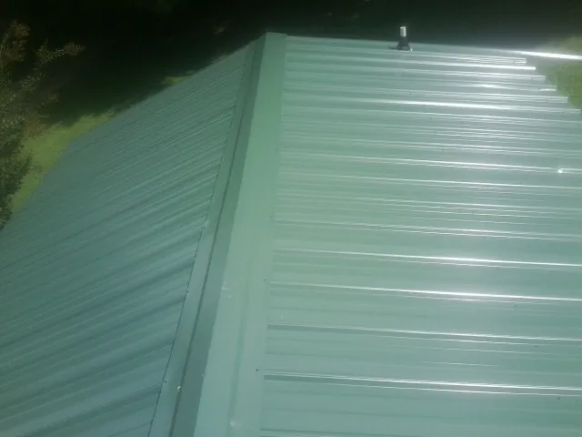 New green metal panels meeting at the ridge of a roof — Flat Roof Repair work by our crew in Pursglove
