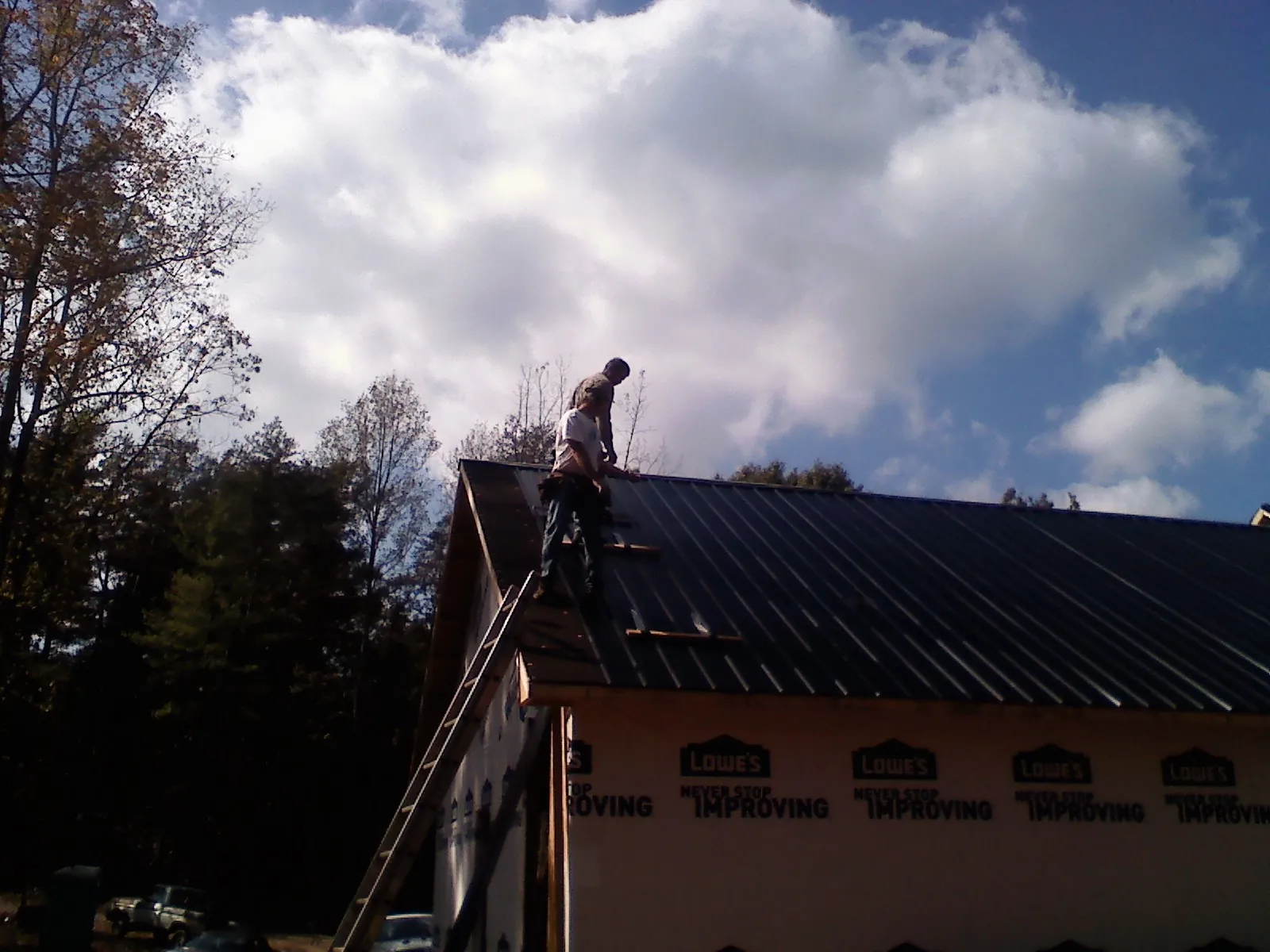 Roofer fastening dark metal panels high against a cloudy sky, from a Roof Inspection job in Pursglove