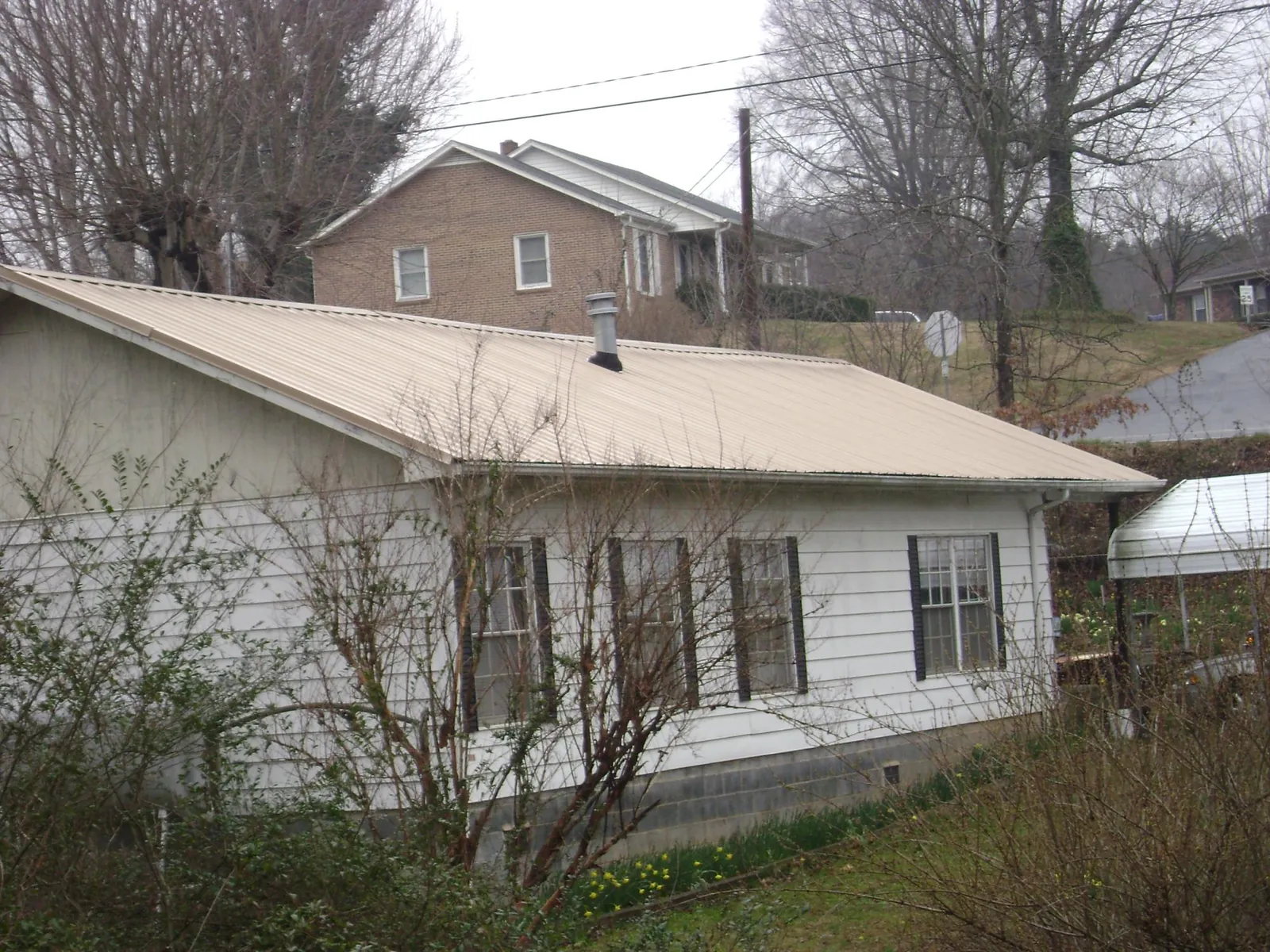 Tan metal roof on a white sided house set into a hillside — Commercial Roofing by Roofing Brothers in Pursglove