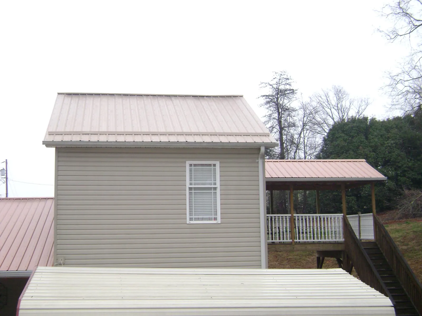 Tan metal roofs on a two story addition and attached porch, from a Roof Replacement job in Pursglove
